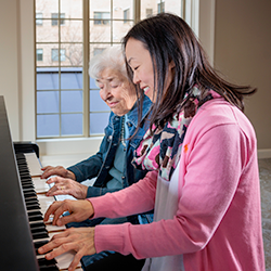 resident playing a piano with a staff member